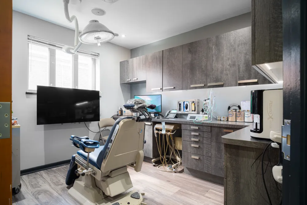 Surgical suite with overhead light, wall-mounted television, and patient chair